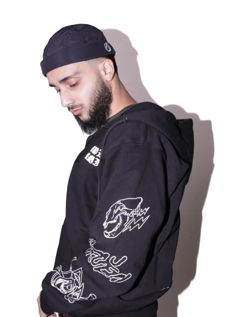 Model menunduk, tampak samping, memperlihatkan sablon tengkorak dan petir di lengan hoodie