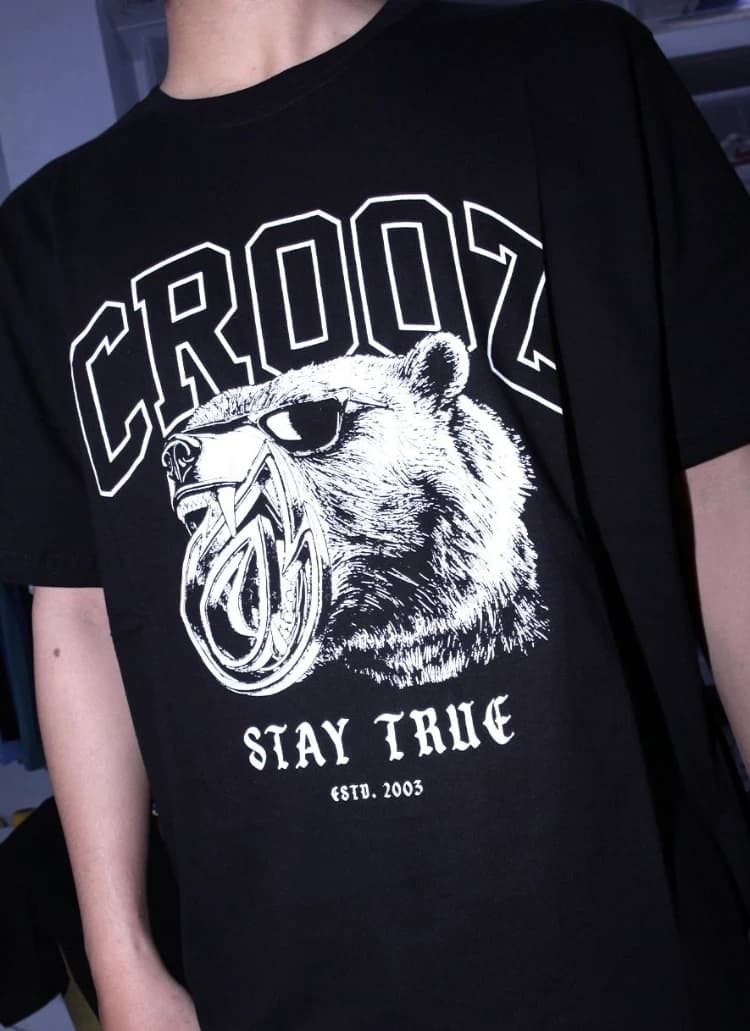 Kaos hitam bergrafis beruang berkacamata menggigit ikon flame, tulisan CROOZ varsity, Stay True dan Estd. 2003