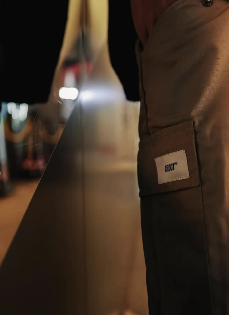 Woven label putih bertuliskan CROOZ di kantong celana cargo khaki