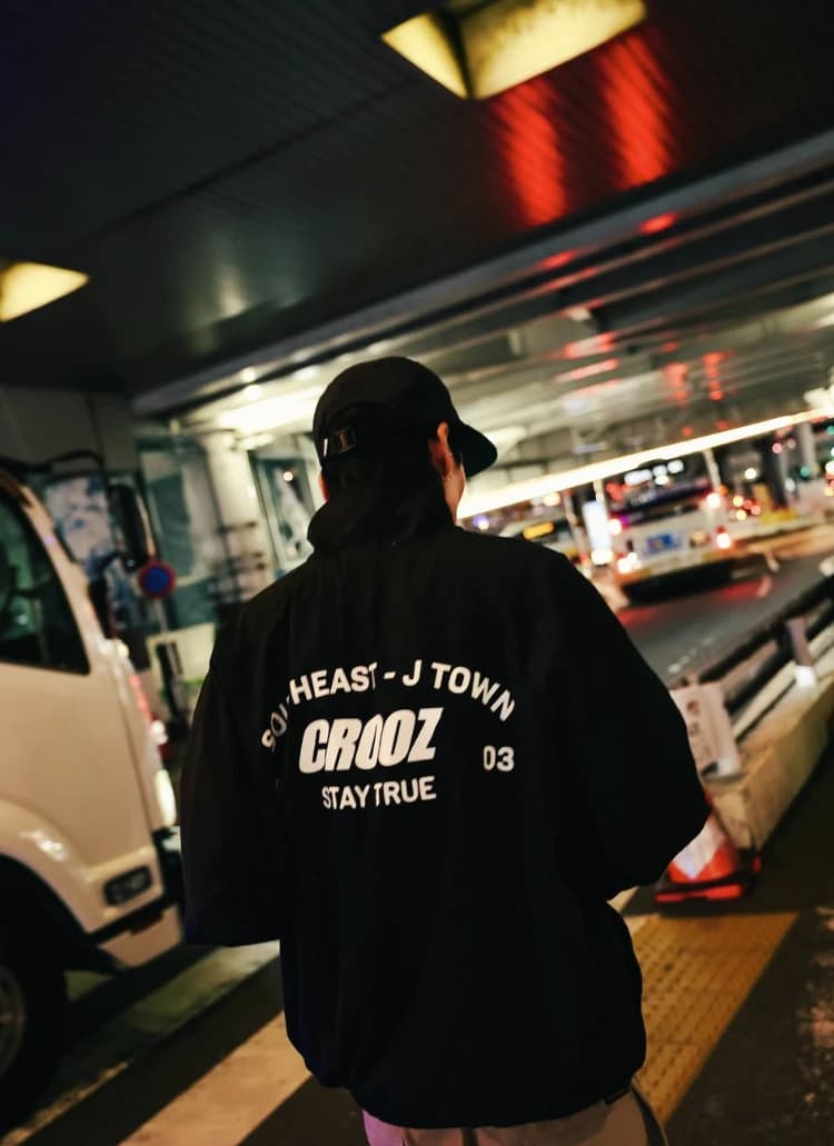 Punggung jaket bertuliskan Southeast J Town, CROOZ, 03, Stay True di terminal bus malam